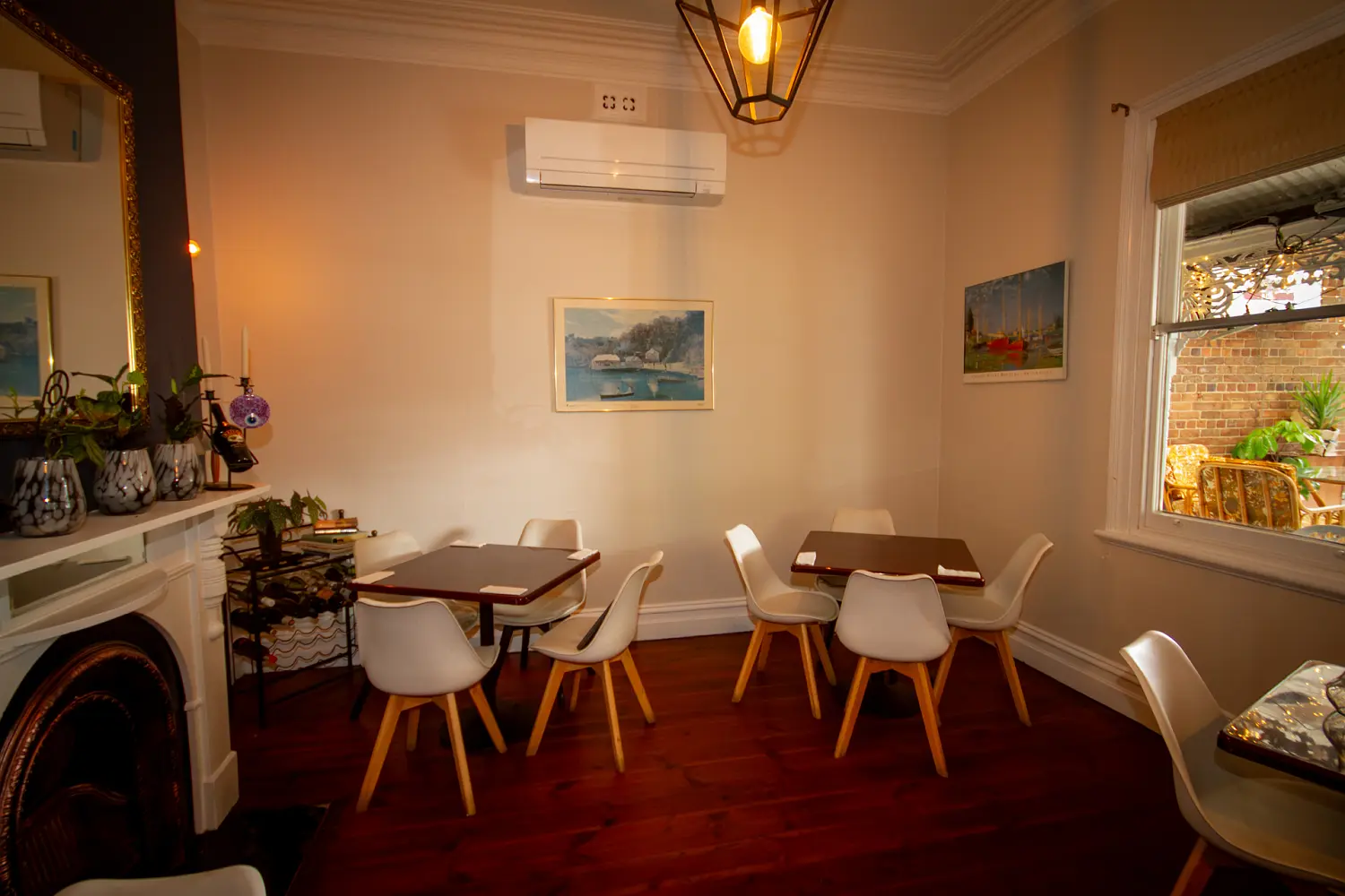 Bright front dining room with modern white chairs, simple table settings and light neutral walls next to a large window.