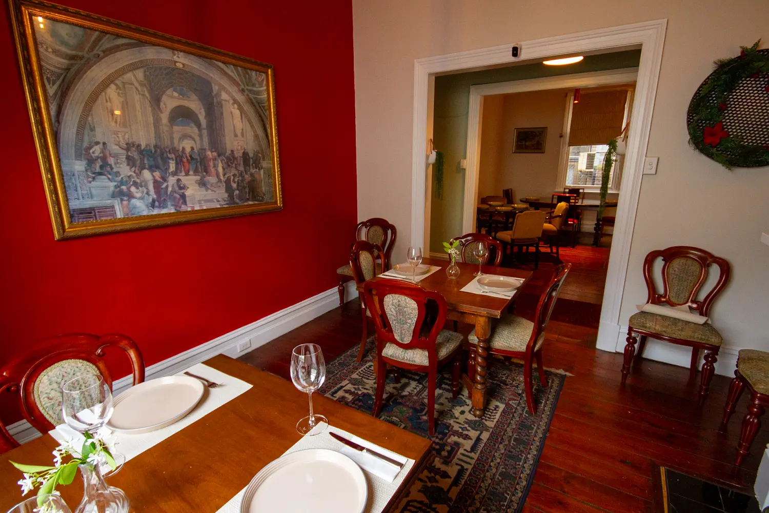 Connected dining rooms with traditional wooden furnishings, red accents, framed artwork and polished timber floors.